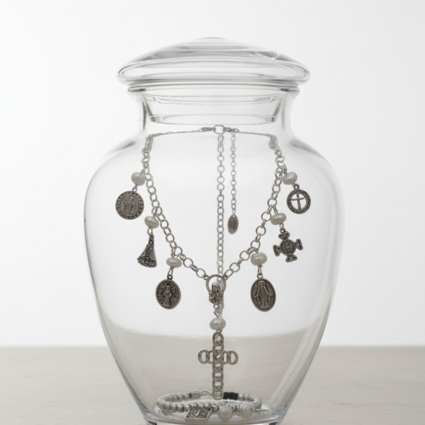 Collar San Benito de Maldita Rita joyería, medallitas con perlas naturales, en una urna de cristal junto a pulsera San Benito.