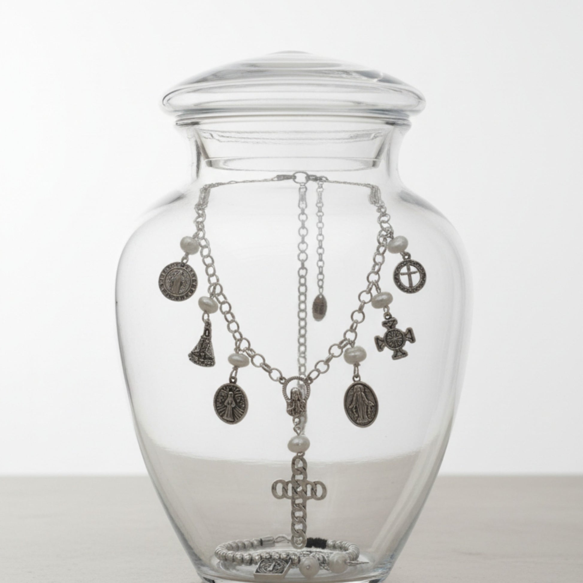 Collar San Benito de Maldita Rita joyería, medallitas con perlas naturales, en una urna de cristal junto a pulsera San Benito.