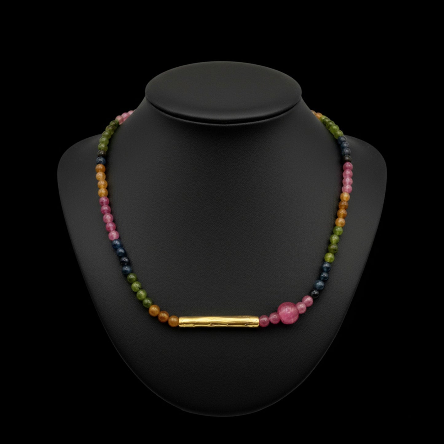 Gargantilla de piedras naturales en diferentes colores y tubo dorado, de Maldita Rita Joyería. En expositor negro