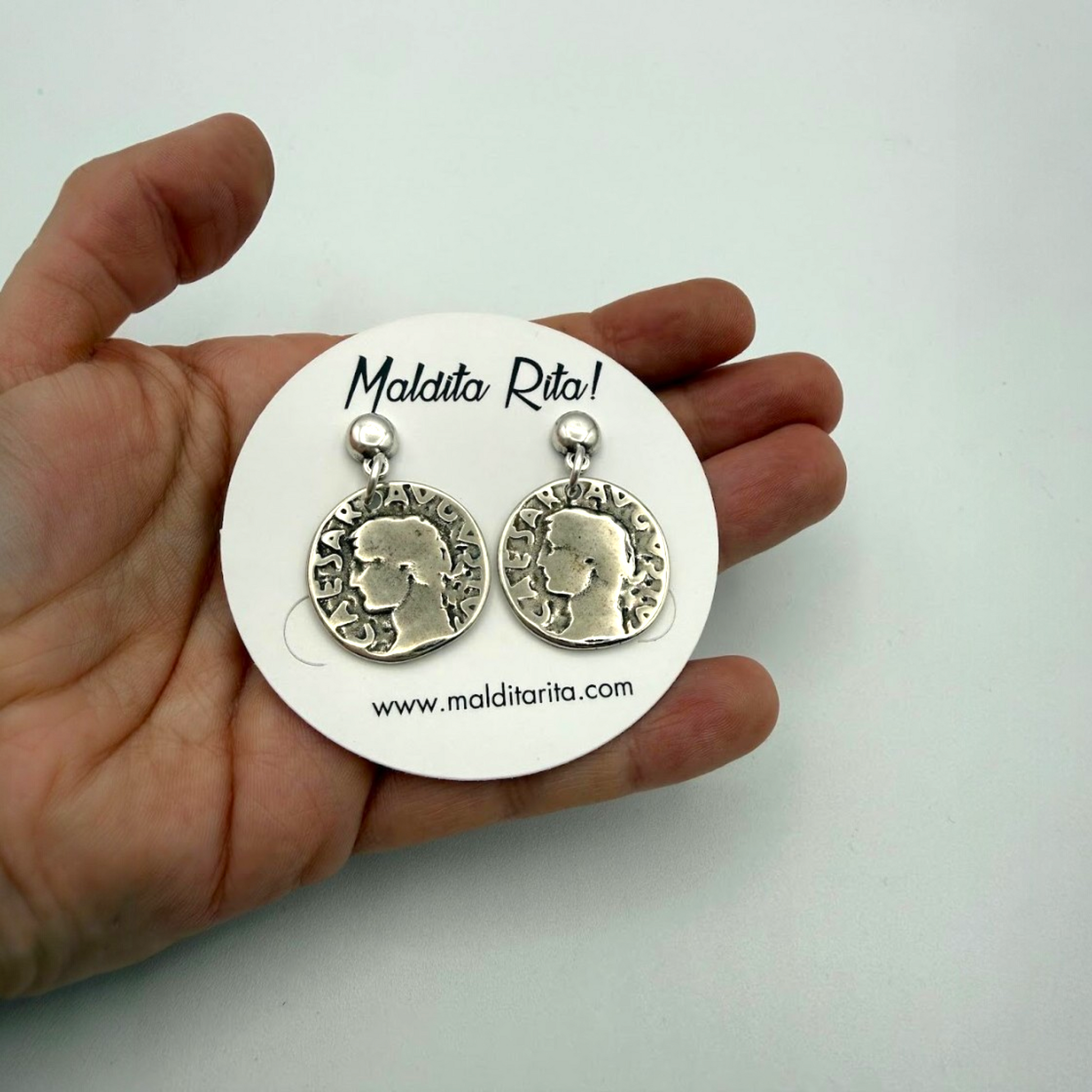 Pendientes de moneda plata antigua de Maldita Rita vistos en la mano.