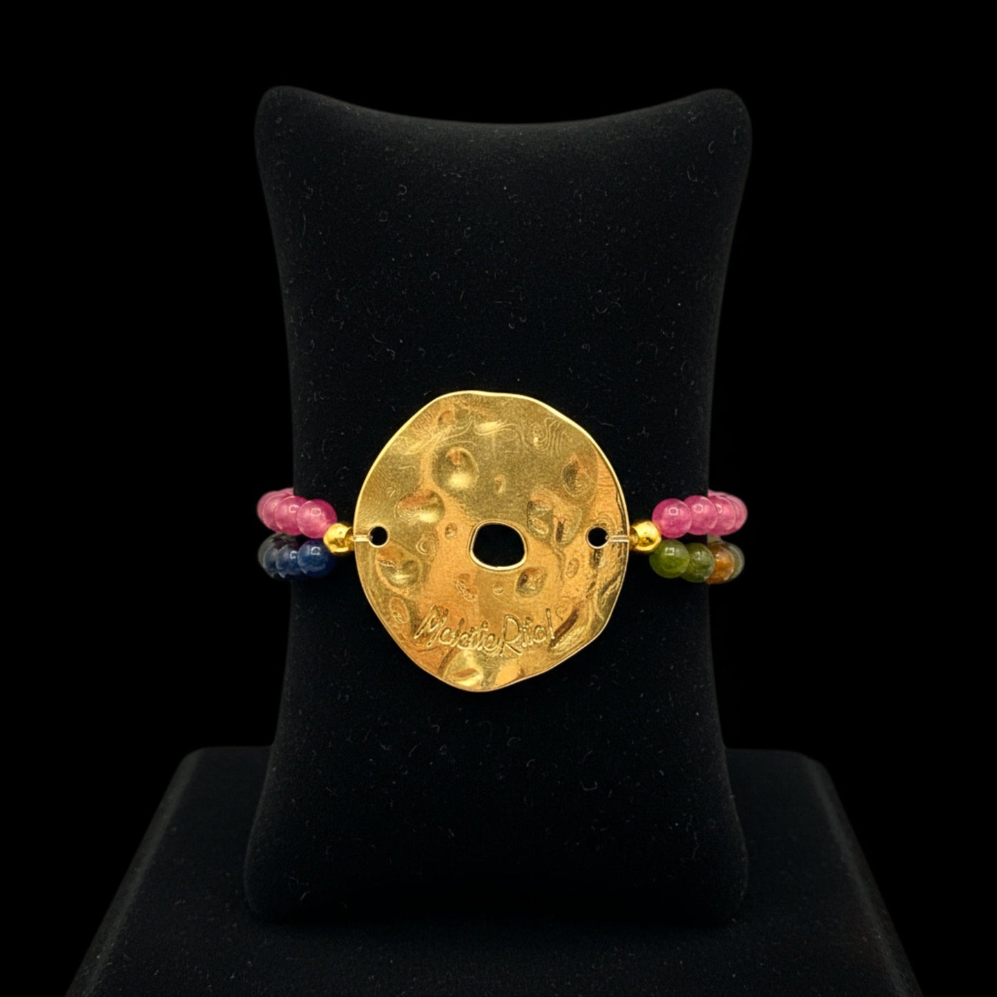 Pulsera elástica con piedras naturales y pieza dorada con logo de Maldita Rita joyería, en expositor negro