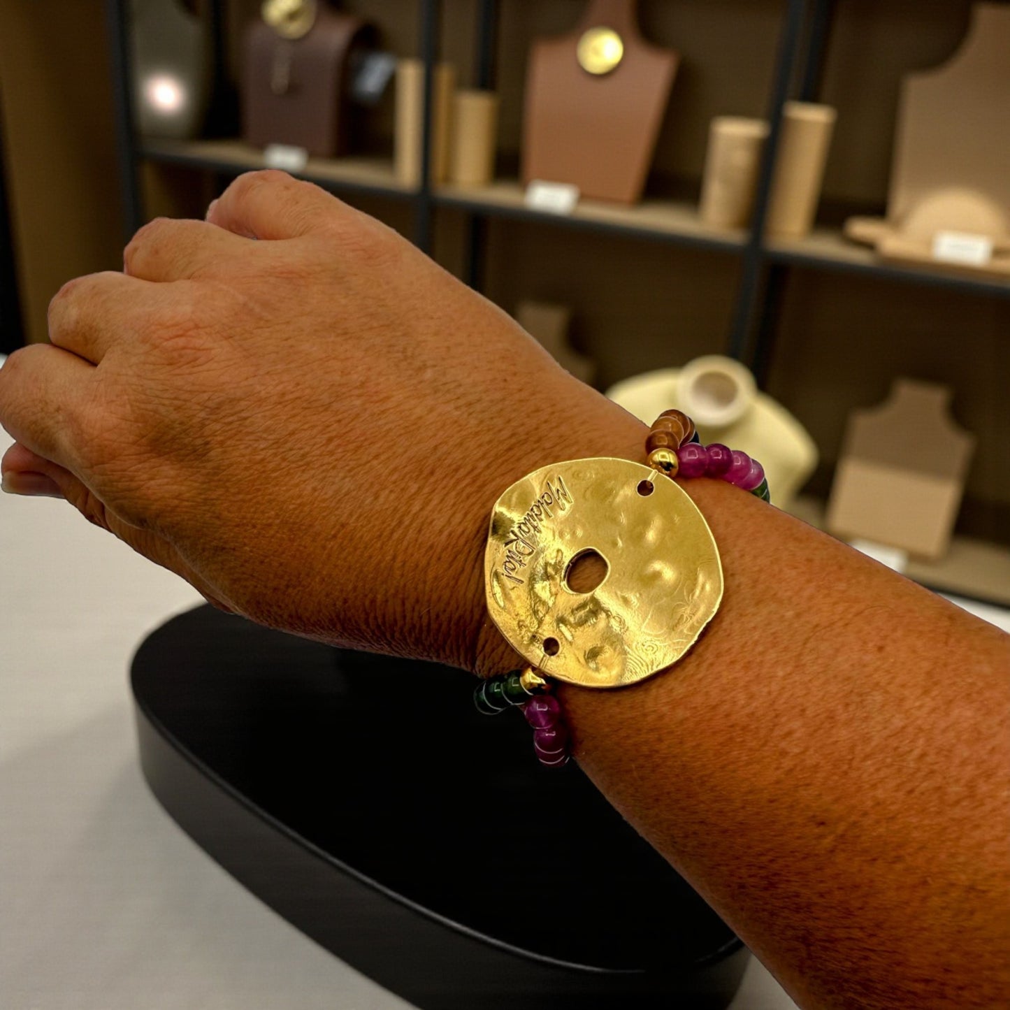 Pulsera elástica con piedras naturales y pieza dorada con logo de Maldita Rita joyería, vista en la muñeca