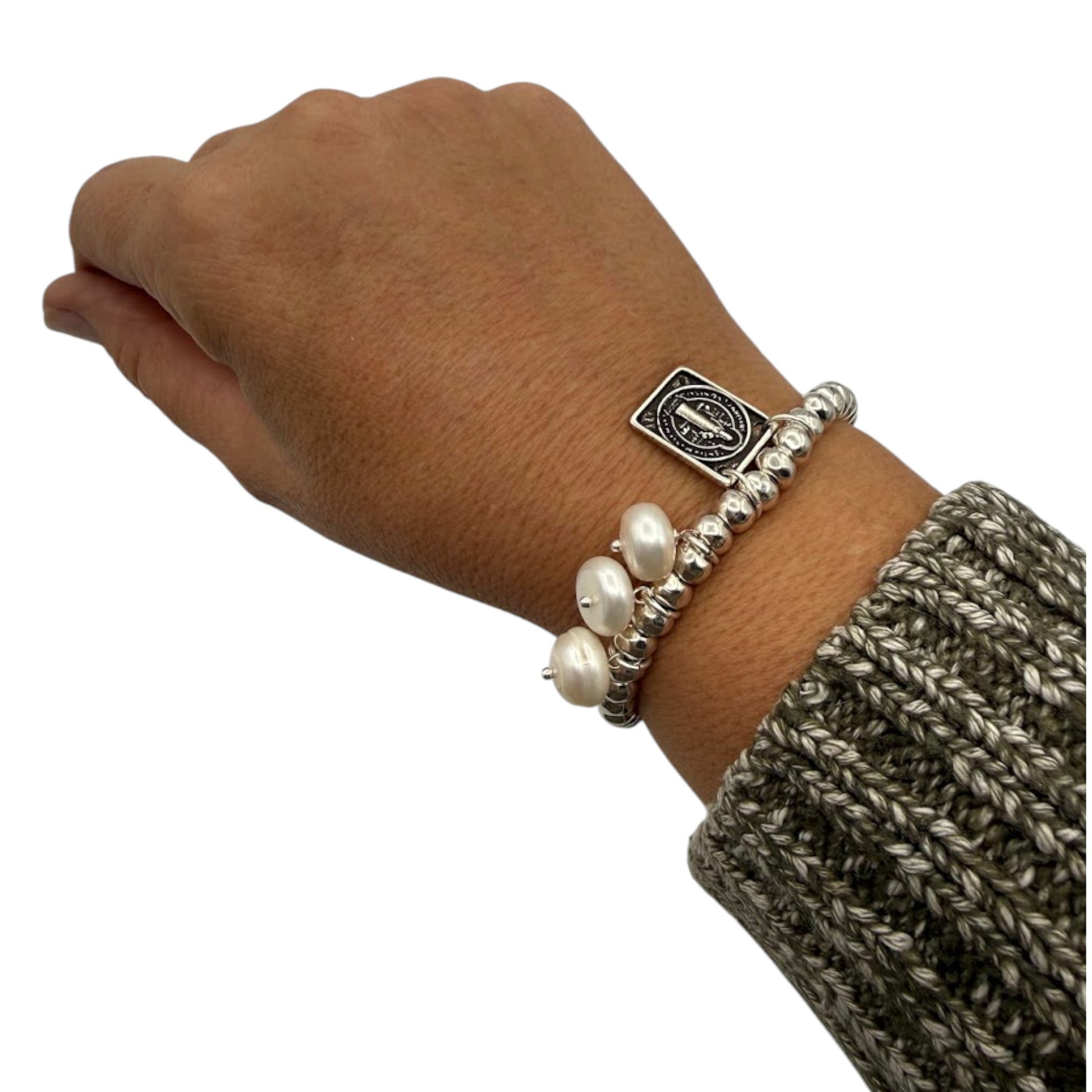 Pulsera con cuentas en plata, medalla de San Benito y perlas blancas naturales, de la marca de joyas de Almería Maldita Rita, en la muñeca.