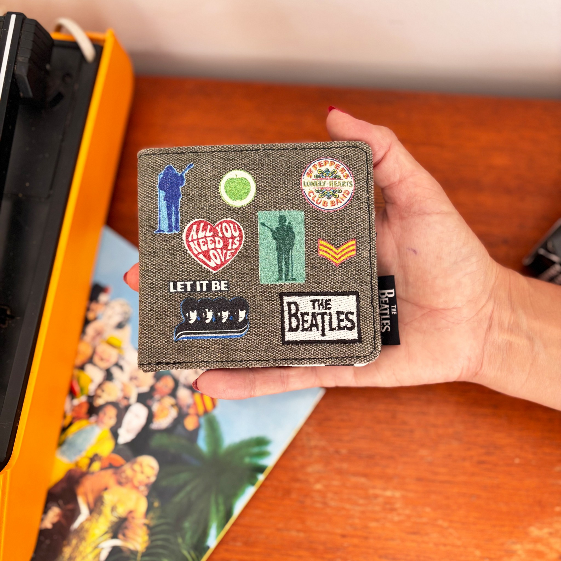 Billetera denim de The Beatles con parches bordados inspirados en Sgt. Pepper, Let It Be y All You Need Is Love. Venta en Maldita Rita, vista en la Mano